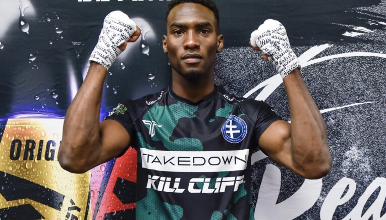 Adamu Isa has his hands taped and is ready to fight as he poses for a photo in front of a sponsored banner
